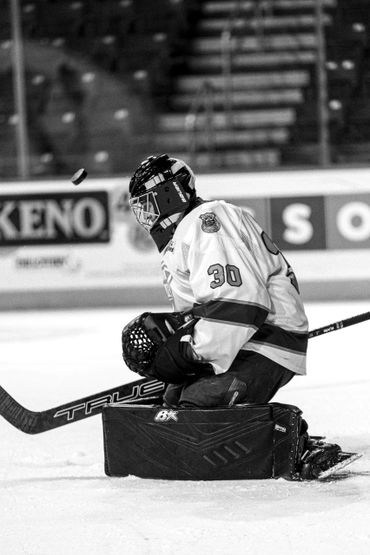 Ice hockey goalie in action, focused on stopping the puck.