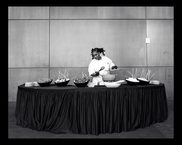 Chef preparing food at a buffet table with skewered items.