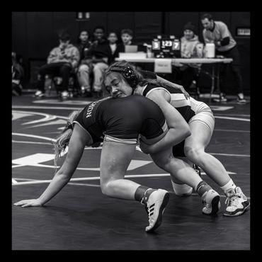 Two female wrestlers competing intensely on the mat during a match.