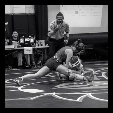 Two female wrestlers compete intensely on the mat with a referee watching closely.