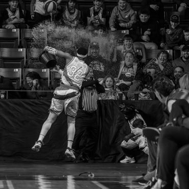 Basketball player splashes water on referee and crowd during a game.