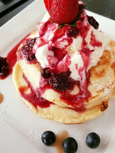 Delicious double pancakes topped with vanilla ice cream, berry compote, and fresh strawberries.