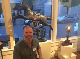 Man posing next to metal horse sculpture in an art gallery.