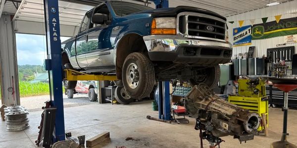 Blue Ford F-250 truck lifted in a garage with its transmission removed.