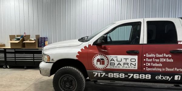 A white and red pickup truck with advertising for The Auto Barn used parts.
