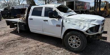 A white Dodge Ram 2500 truck with severe front and roof damage.