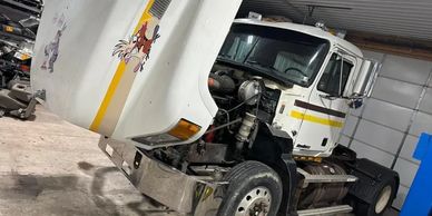 White semi-truck with raised hood featuring cartoon decals in a garage.