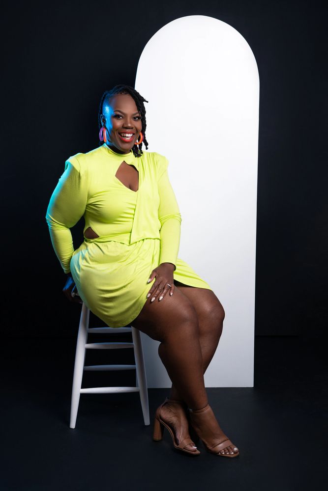 Woman in neon dress sitting on stool.
