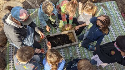Students and their teacher gather around a worm bin in their Garden Science class.