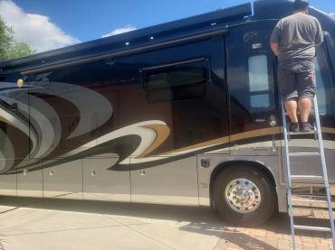 Person on ladder working on a large black RV.