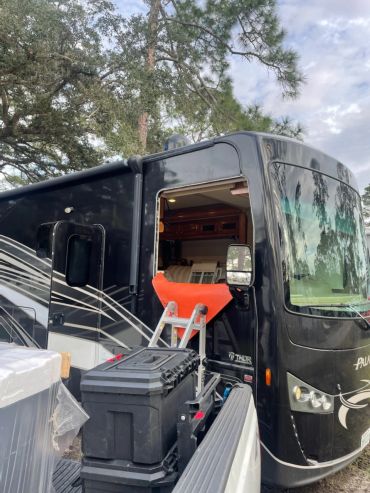 Black RV with open front window and ladder.