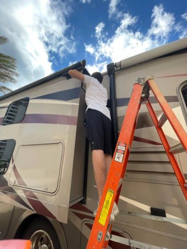 Person on ladder fixing or adjusting an RV awning.