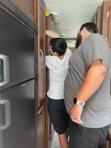 Two men working on a cabinet inside a narrow space.