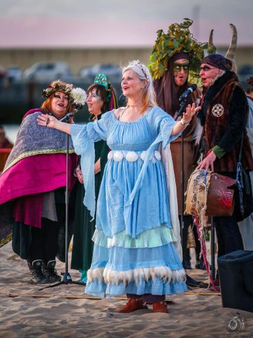 A group of people in colorful fantasy costumes performing on a sandy beach.