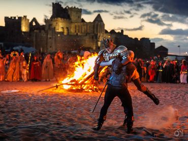 Medieval-themed battle reenactment by a bonfire with an ancient castle in the background.
