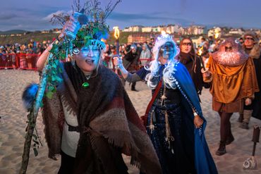 People dressed in fantasy costumes holding torches at a beach event.