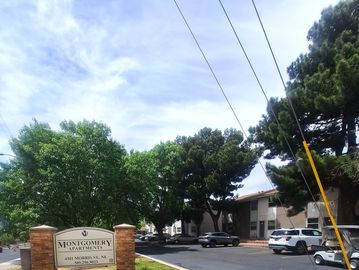 Montgomery Apartments entrance with trees and parked cars under a partly cloudy sky.