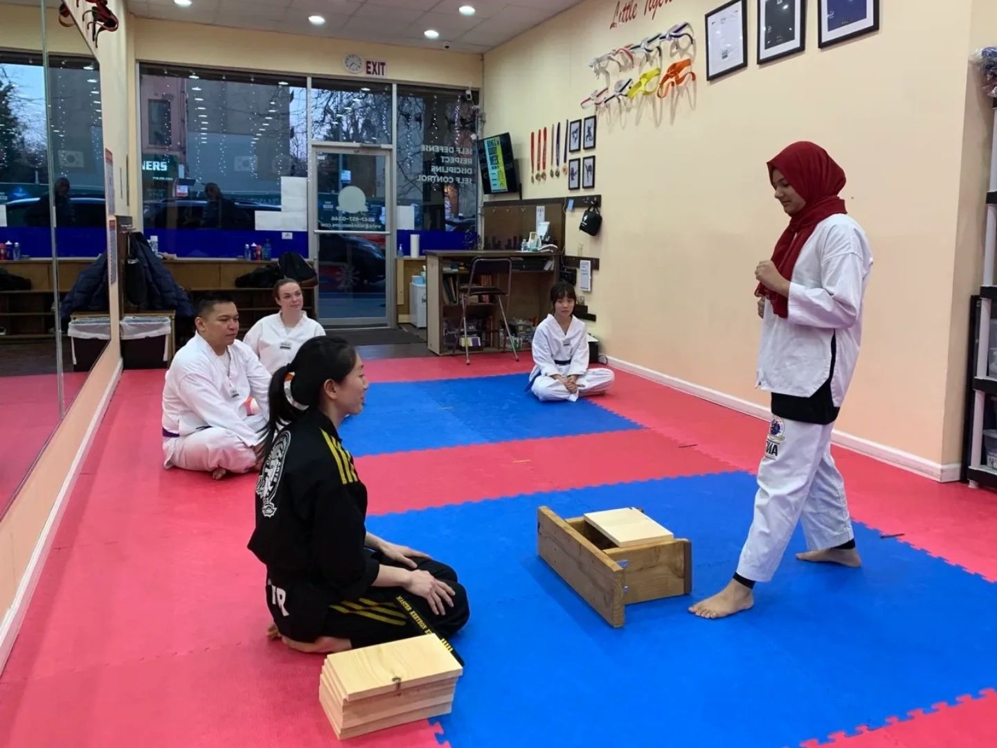 Martial arts students gather in a dojo with wooden boards for breaking practice.