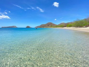 Crystal-clear water meets a tranquil sandy beach under a bright blue sky.