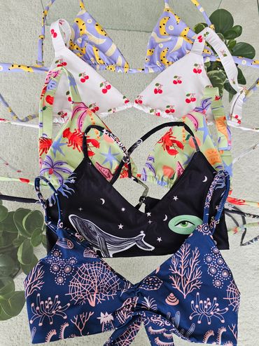Colorful patterned bikini tops laid out on a flat surface with a plant nearby.