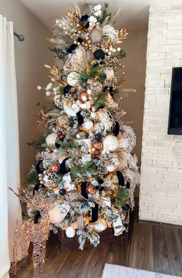 Luxuriously decorated Christmas tree with gold, black, and white ornaments and a lit reindeer figure.
