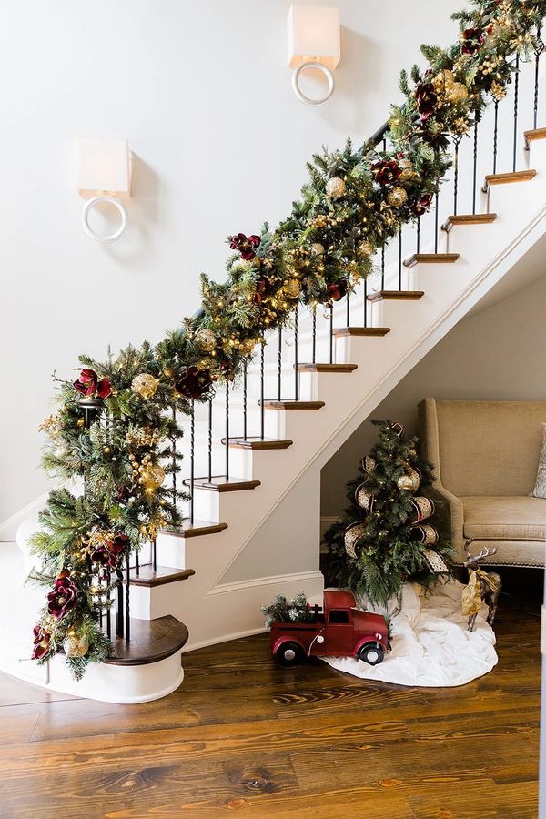 Festive Christmas garland decorates stair railing with a red toy truck and small tree underneath.