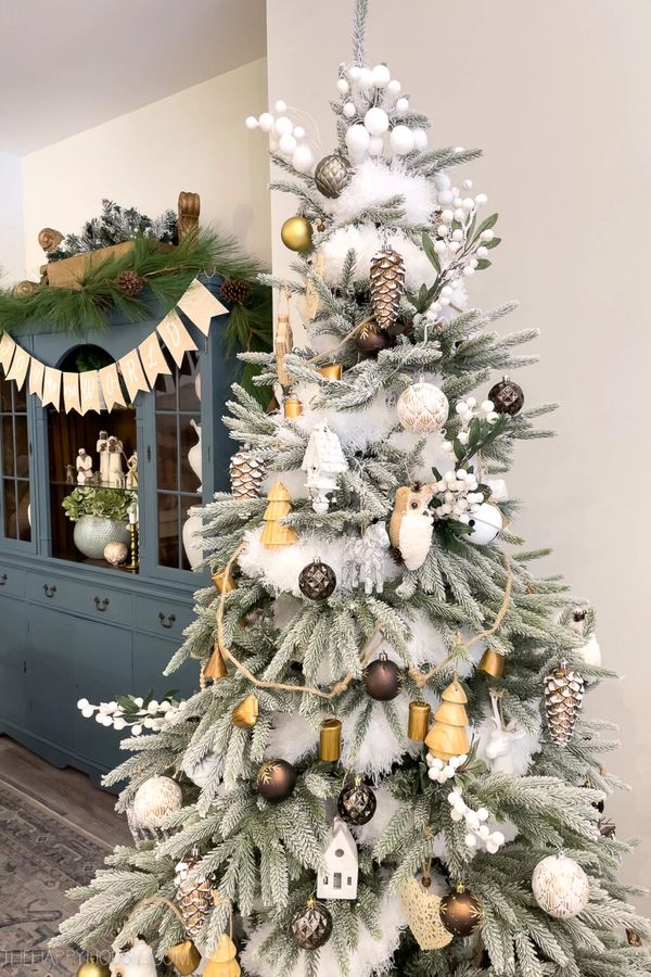 Elegant Christmas tree with white, gold, and brown ornaments in a cozy living room.