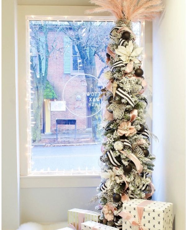 Tall, narrow Christmas tree decorated with black, white, and pink ornaments.