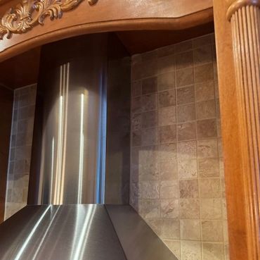 Stainless steel kitchen range hood with wooden trim and tiled backsplash.