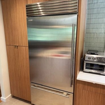Stainless steel refrigerator integrated into wooden kitchen cabinetry.