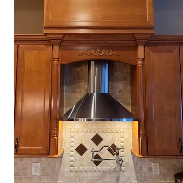 Modern kitchen stove with stainless steel hood and wooden cabinets.