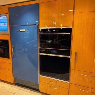 Modern kitchen with wood cabinets, blue refrigerator, and built-in ovens.