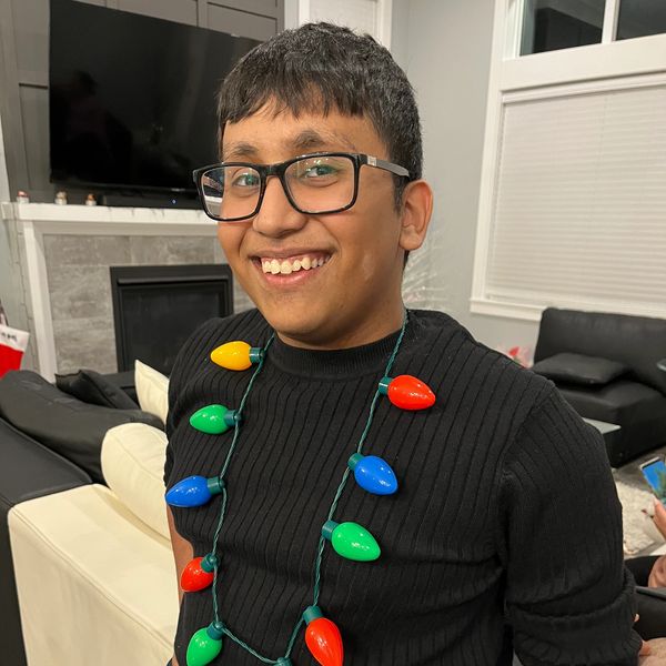 A smiling young man wearing glasses and a necklace made of colorful Christmas lights.