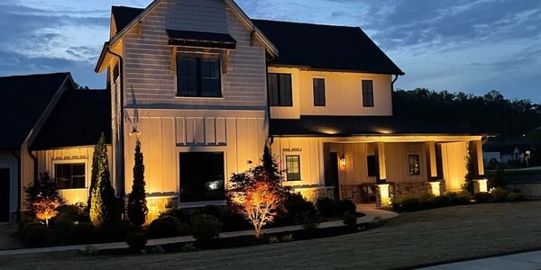 A beautifully lit modern farmhouse at dusk with warm exterior lighting.