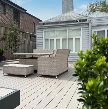 Modern outdoor patio with wicker furniture and light wooden decking.