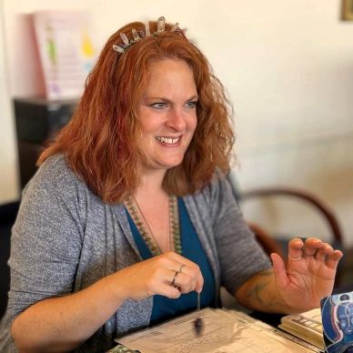 A woman with red hair smiling while holding a pendulum over a paper.