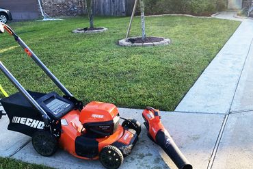 Orange Echo lawn mower and leaf blower on a driveway beside a green lawn.