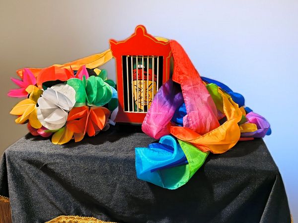 Colorful paper flowers and a red cage decoration on a black cloth with gold fringe.