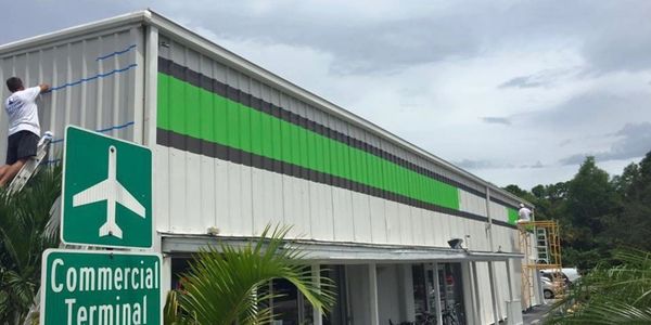 Workers paint green and black stripes on a commercial terminal building.