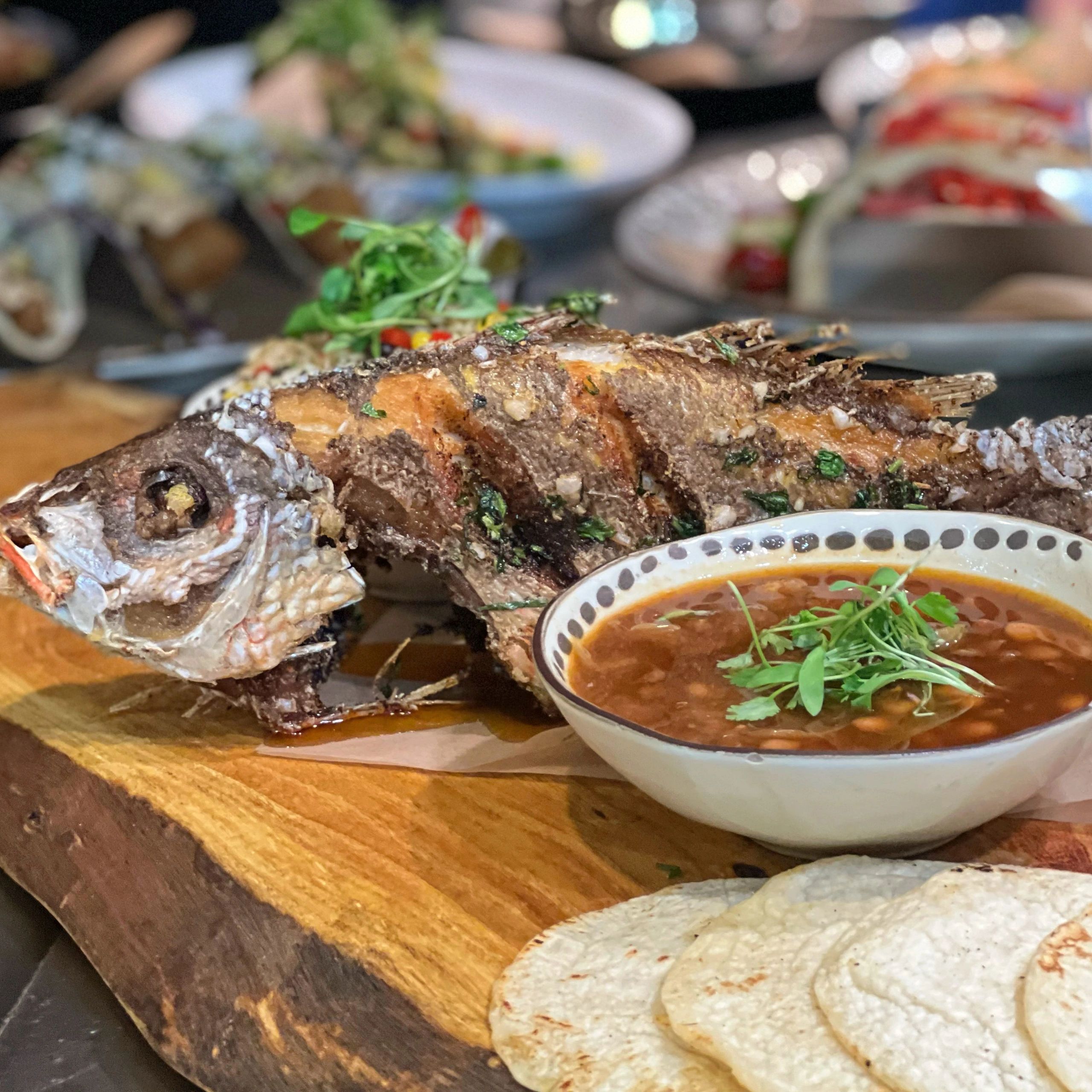 Crispy whole fish served on a wooden plank, with tortillas and pinto beans