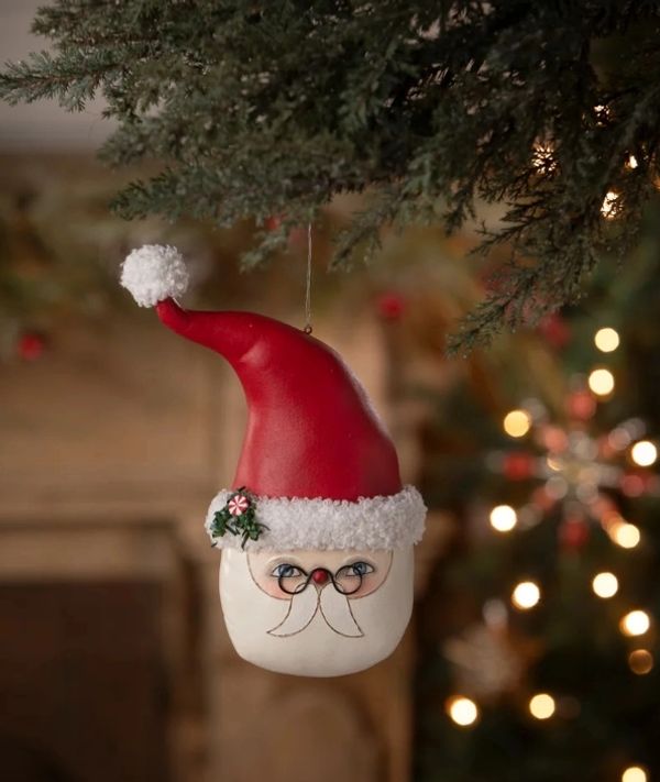 Santa Claus face ornament hanging on a Christmas tree branch.