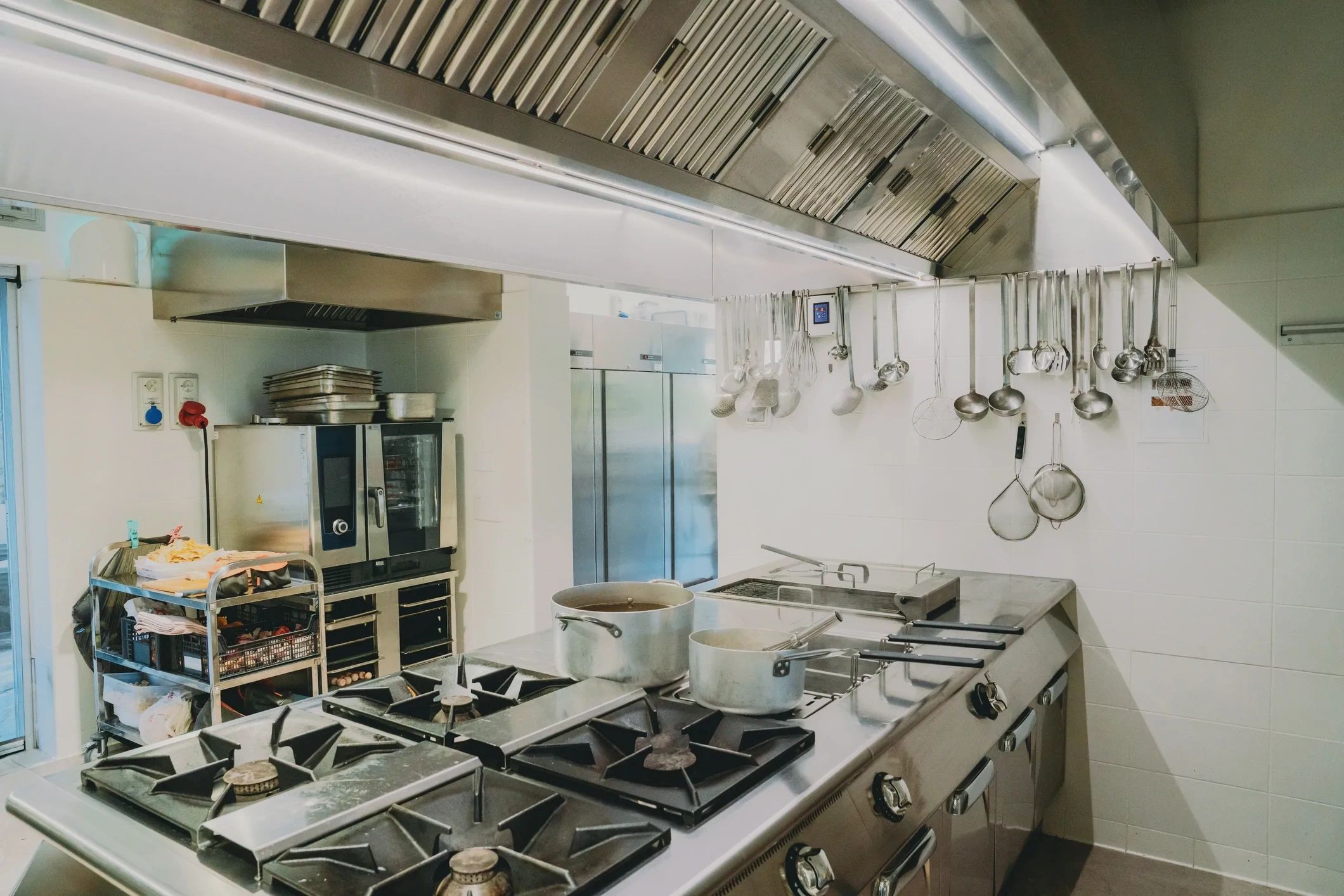 Commercial kitchen with cooking utensils and pots on stove.