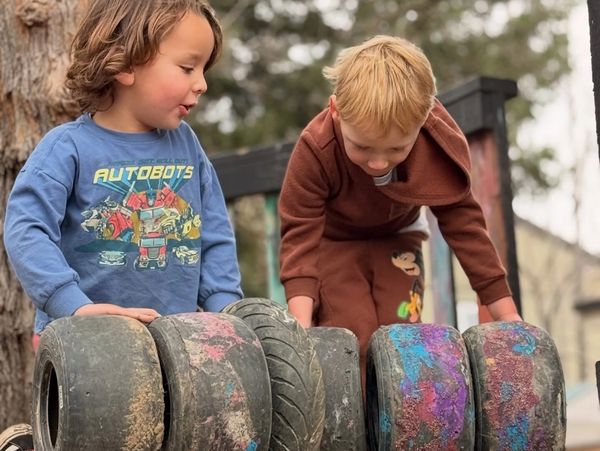 Two boys playing with large painted tires outdoors.