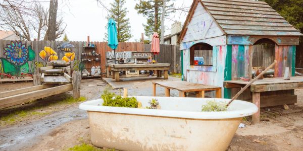 Outdoor play area with a bathtub planter and a wooden playhouse.