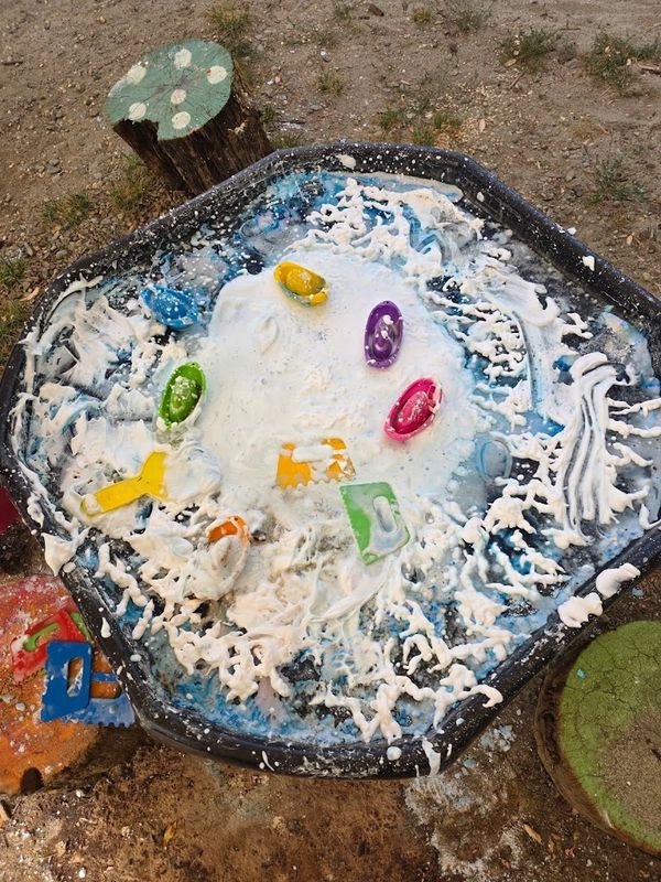 Outdoor sensory table with foam and colorful tools.