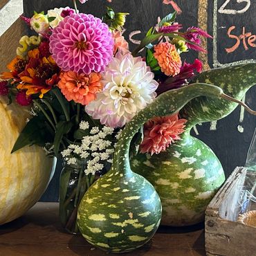 Colorful flowers in a jar with gourds and a pumpkin on a wooden table.