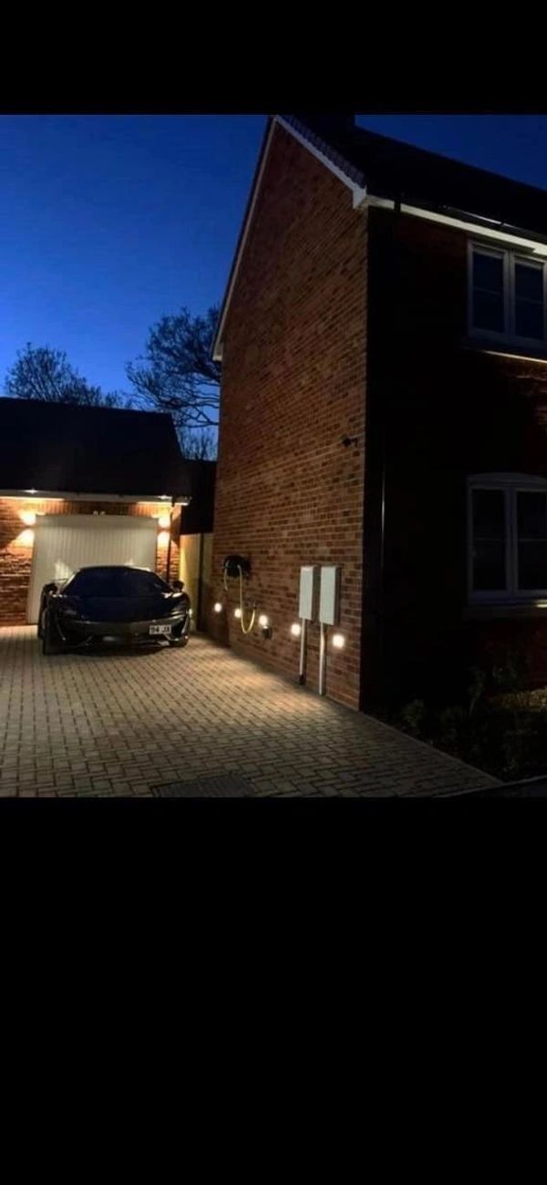 A modern brick house illuminated by warm outdoor lights at night with a car parked in the driveway.