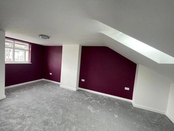 Empty room with purple accent walls and gray carpet under sloped ceiling.