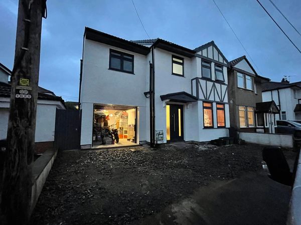 A semi-detached house with an open garage and illuminated windows at dusk.