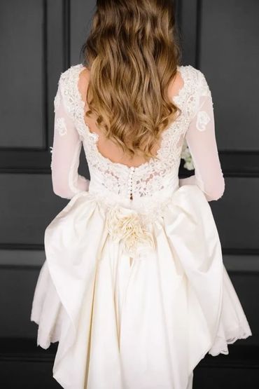Bride in a lace wedding gown with long wavy hair and a large bow at the back.